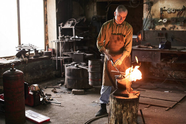 Blacksmith heats the gas burner over metal product on the anvil