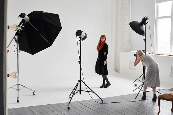 Girl photographer photographing fashion model in black color on white background in Studio