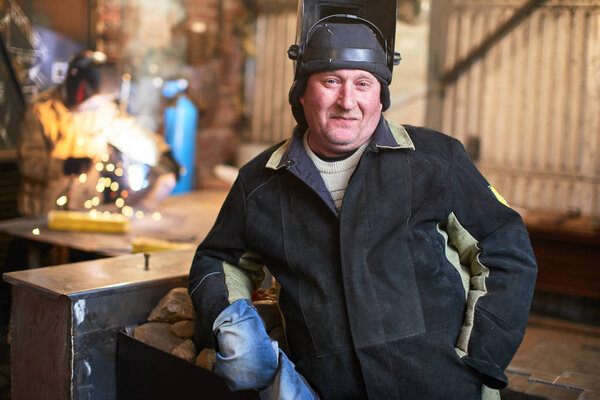 welder wearing safety equipment looking at camera while standing at factory 