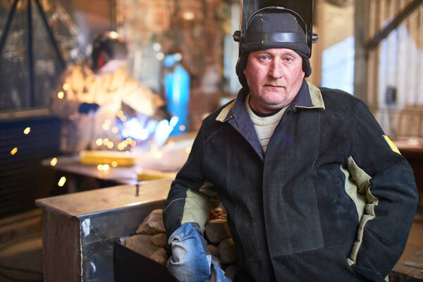 welder wearing safety equipment looking at camera while standing at factory 