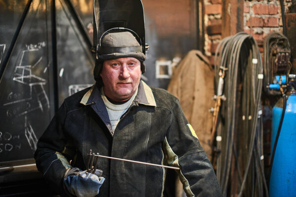 serious welder wearing welding mask holding welding machine standing at workshop 