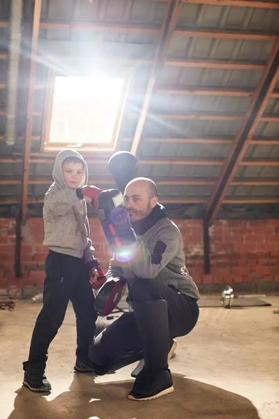 Father in sport suit with son working out boxing blow in makeshift home gym