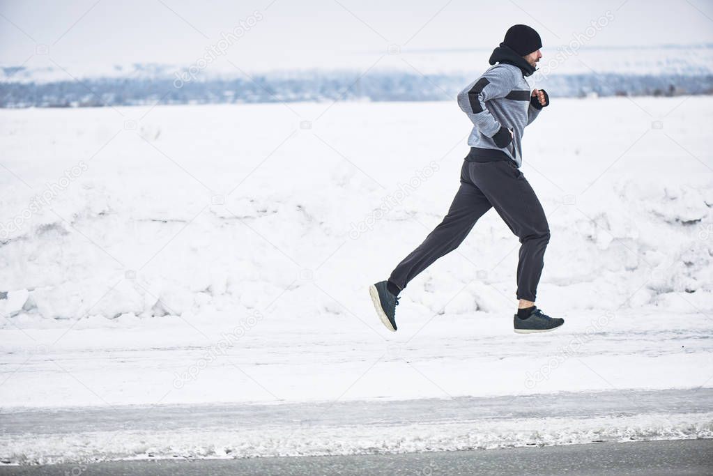side view of sportsman in warm sportswear running on highway in cold early morning 