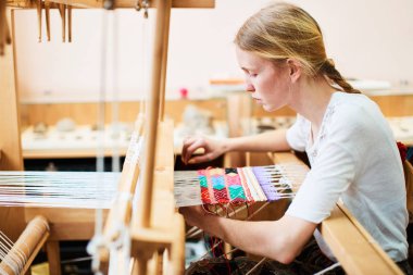 üretim sürecinde Tekstil dokuma tezgahı üzerinde el yapımı profesyonel sarışın kadın 
