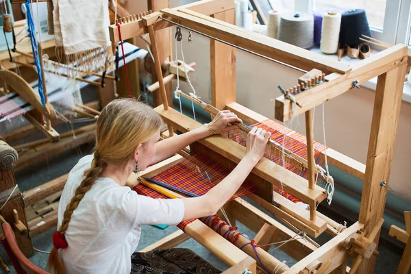 professional blonde woman in production process of textiles handmade on loom