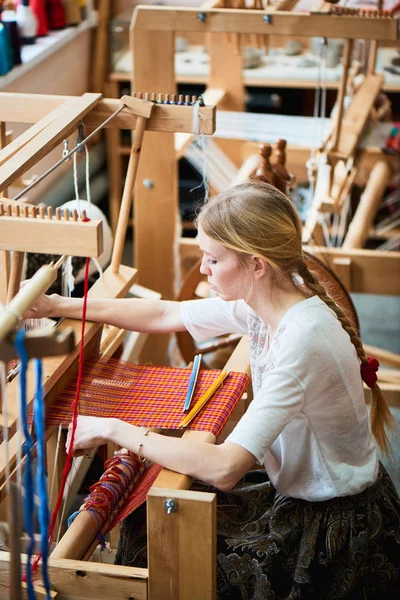 professional blonde woman in production process of textiles handmade on loom