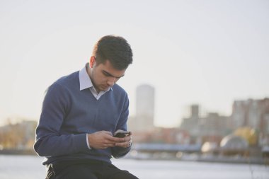 kazak ve gömlek riverside adlı dururken smartphone kullanarak yakışıklı işadamı