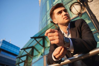 işadamı korkuluk ve akıllı saati cam bina ve zemin üzerine mavi gökyüzü ile eğilerek takım elbiseli 