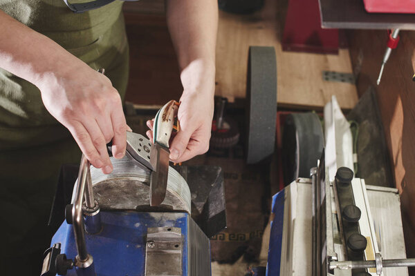 Close-up view of male hands sharpening the knife at workshop