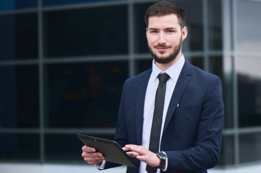 yakışıklı işadamı arka plan üzerinde Mimari camlar ile tablet pc kullanarak kameraya bakıyor 