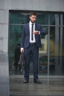yandan iş binanın verandada duran bakarak evrak çantası ile takım elbiseli yakışıklı işadamı