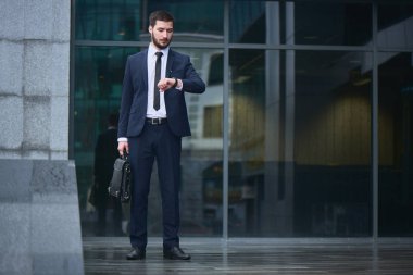 yandan iş binanın verandada duran bakarak evrak çantası ile takım elbiseli yakışıklı işadamı