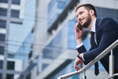 arka planda bina ile korkuluk üzerine yaslanmış iken Evet takım elbiseli yakışıklı işadamı