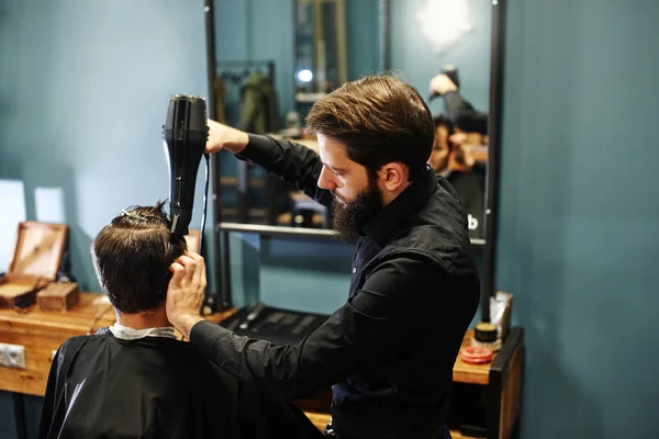 Barber man in the black shirt in the process of cutting a customer in the barbershop