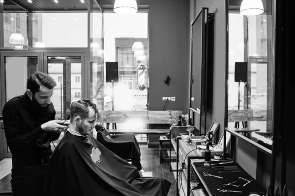 Black and white photo of barber man in the black shirt in the process of cutting a customer in the barbershop