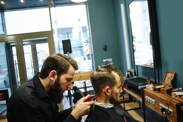 Barber man in the black shirt in the process of cutting a customer in the barbershop