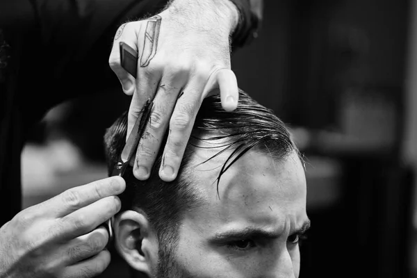 Black and white photo of barber man in the black shirt in the process of cutting a customer in the barbershop