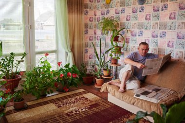 kanepede oturan ve evde gazete okurken yetişkin adam 