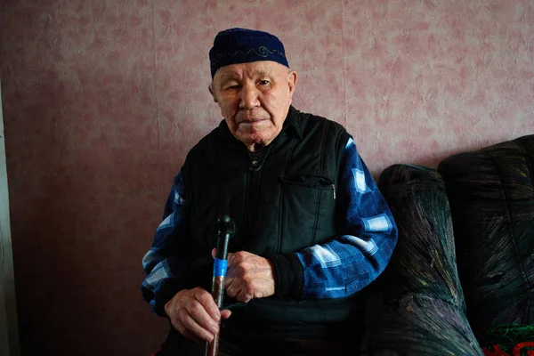 asian man with walking stick sitting in Kazakh house