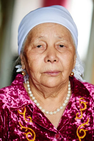 portrait of old Kazakh woman looking at camera on blurred house background