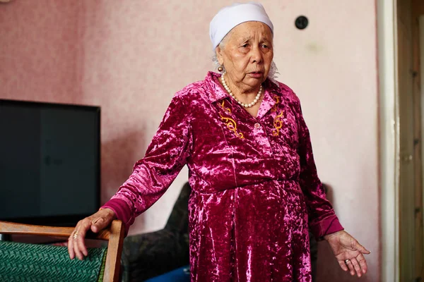 old Kazakh woman in pink robe standing in house