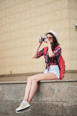fotoğrafta Street mermer parapetin üzerinde otururken elinde kamerayla çekici kadın yan görünüm 