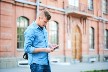 kot gömlek ve kot Üniversitesi önünde duran tablet pc kullanarak yakışıklı öğrenci 
