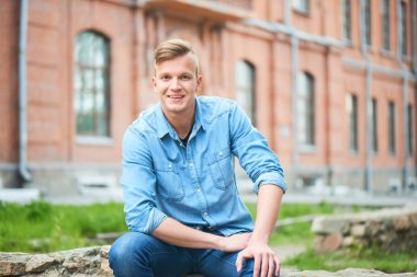 Kot gömlek ve kamera arka planda bina ile tuğla çit oturan süre seyir kot mutlu gülümseyen öğrenci portresi 