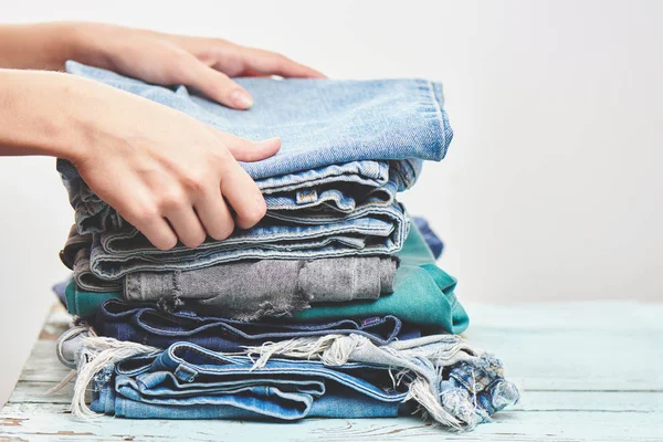 female hands putting pant on stack of blue jeans on wooden background, close-up