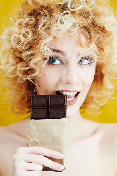 Young Blonde Woman Curly Hair Biting Chocolate Bar Smiling Yellow Royalty Free Stock Photos