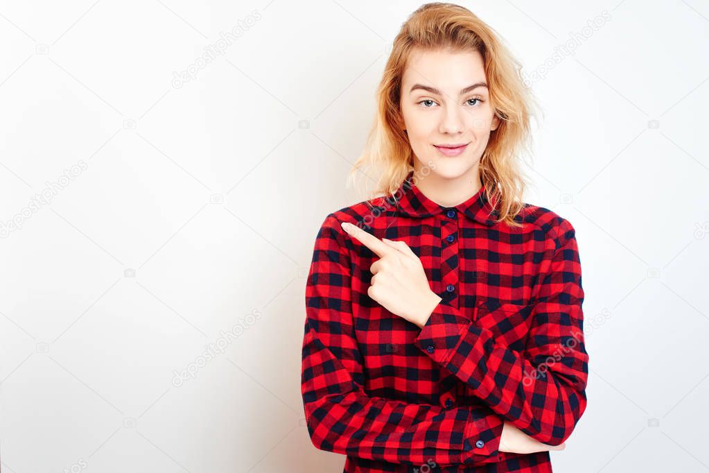 beautiful smiling woman in checkered shirt pointing with finger to left isolated on white background 