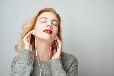 gülümseyen memnun Kızıl saçlı kadın kırmızı dudaklı kulaklık ile müzik dinlemek yakın çekim 