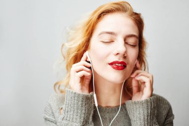 gülümseyen memnun Kızıl saçlı kadın kırmızı dudaklı kulaklık ile müzik dinlemek yakın çekim 