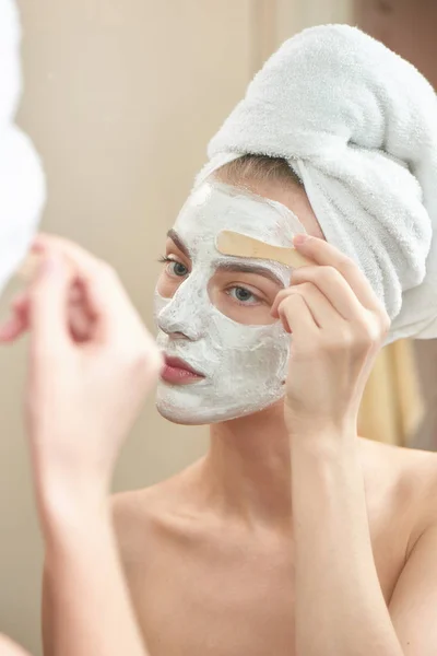 Donna Sorridente Che Indossa Asciugamano Sulla Testa Applicando Maschera Viso — Foto Stock