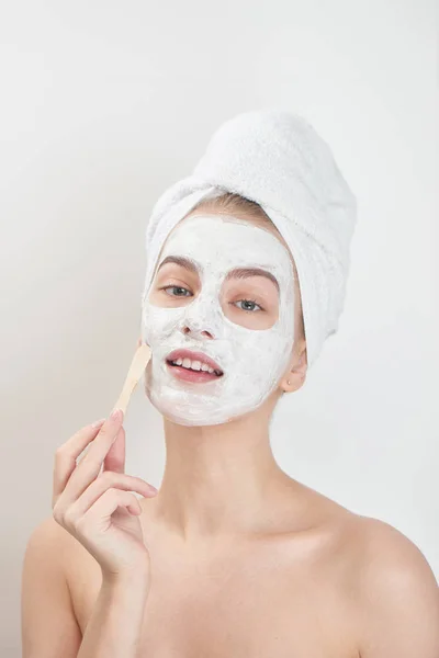 smiling woman wearing towel on head applying face mask with wooden stick , beauty treatment concept