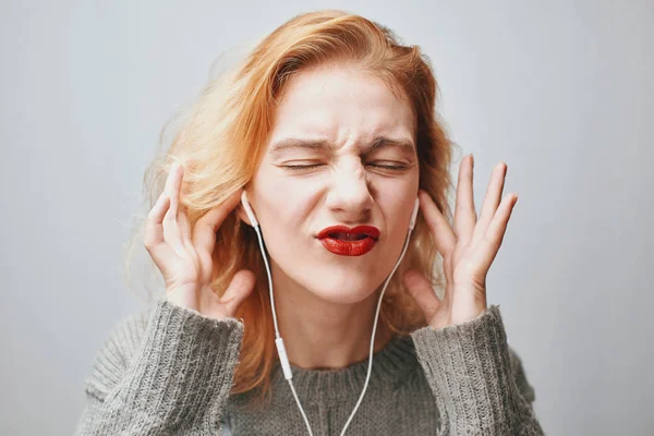 red-haired woman with closed eyes wearing  sweater listening to music with headphones