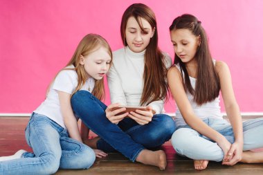 şirin kızlar pembe studio arka plan üzerinde otururken smartphone üzerinde oyun oynamak rahat kıyafetler giymiş
