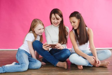 şirin kızlar pembe studio arka plan üzerinde otururken smartphone üzerinde oyun oynamak rahat kıyafetler giymiş
