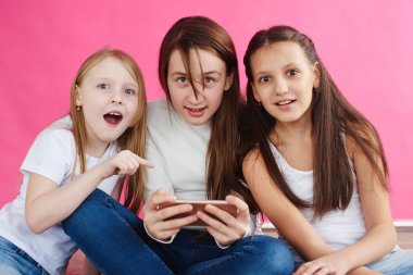şirin kızlar pembe studio arka plan üzerinde otururken smartphone üzerinde oyun oynamak rahat kıyafetler giymiş
