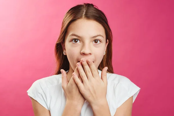 Portrait of surprised girl closed mouth with hands on pink background