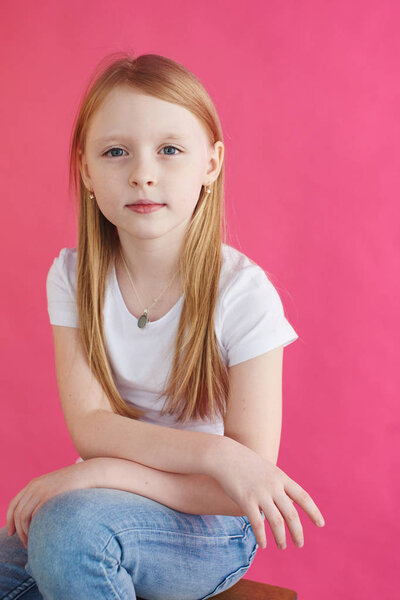 Little blonde girl sitting on wooden chair with pink wall on background