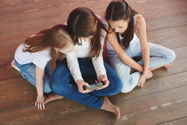 Три Дівчата Підлітки Грають Ігри Телефоні Сидячи Дерев Яній Підлозі — стокове фото