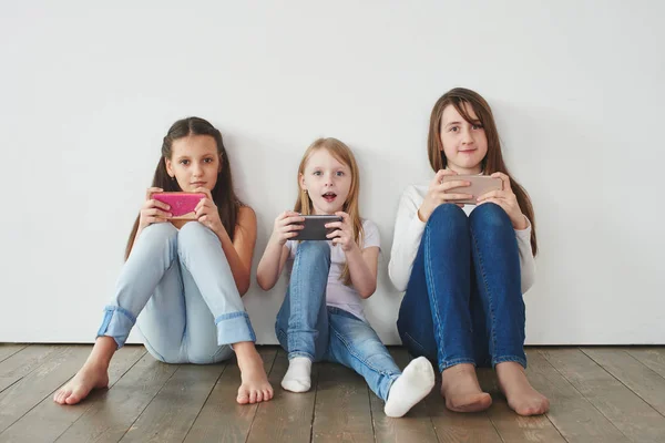 Tres Chicas Apoyadas Pared Blanca Jugando Juegos Teléfonos Inteligentes Concepto —  Fotos de Stock