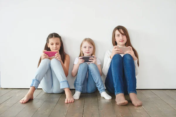 Tres Chicas Apoyadas Pared Blanca Jugando Juegos Teléfonos Inteligentes Concepto —  Fotos de Stock