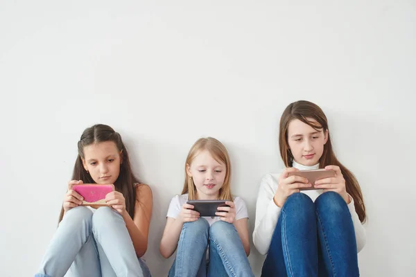 Три Дівчини Спираючись Білу Стіну Граючи Ігри Смартфонах Концепція Азартної — стокове фото