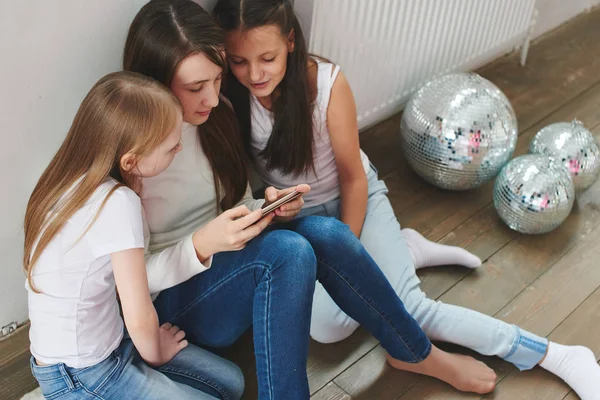 Three girls playing games on phone while sitting on floor near on white wall, Gambling addiction concept