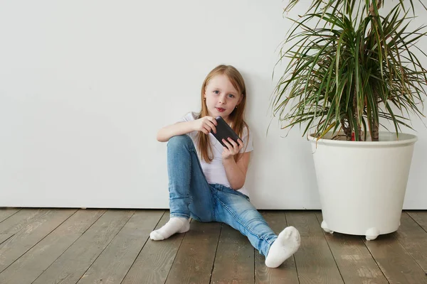 Menina Loira Jogando Telefone Enquanto Sentado Chão Madeira Fundo Branco — Fotografia de Stock