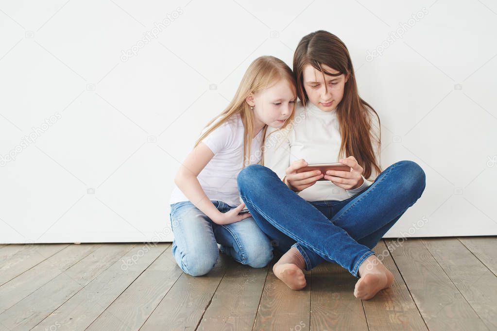 two girls in casual clothes sitting on floor and playing games on smartphone, Gambling addiction concept 