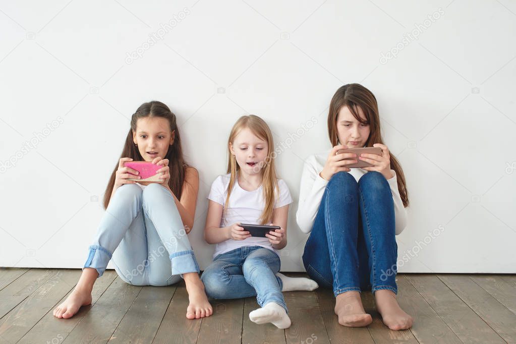 Three girls leaning on white wall and playing games on smartphones, Gambling addiction concept 