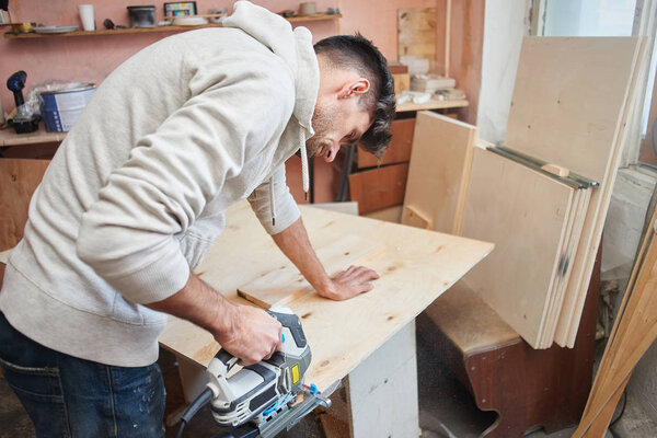 young man working with electric fretsaw while sawing plywood, concept of make repairs in apartment 